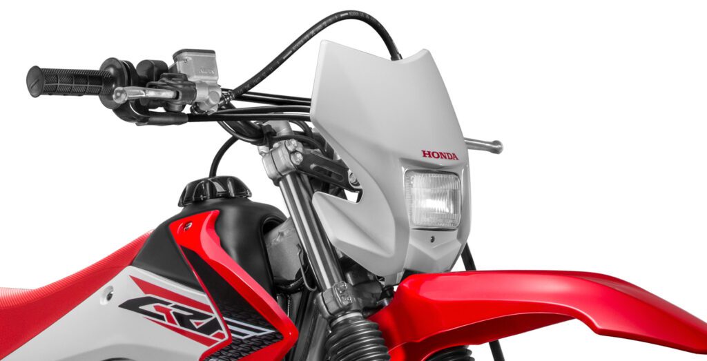 fotografia mostrando a parte da frente da moto honda crf 230 focando no farol, guidão, manetes de freio e embreagem, paralama dianteiro e tanque de combustível